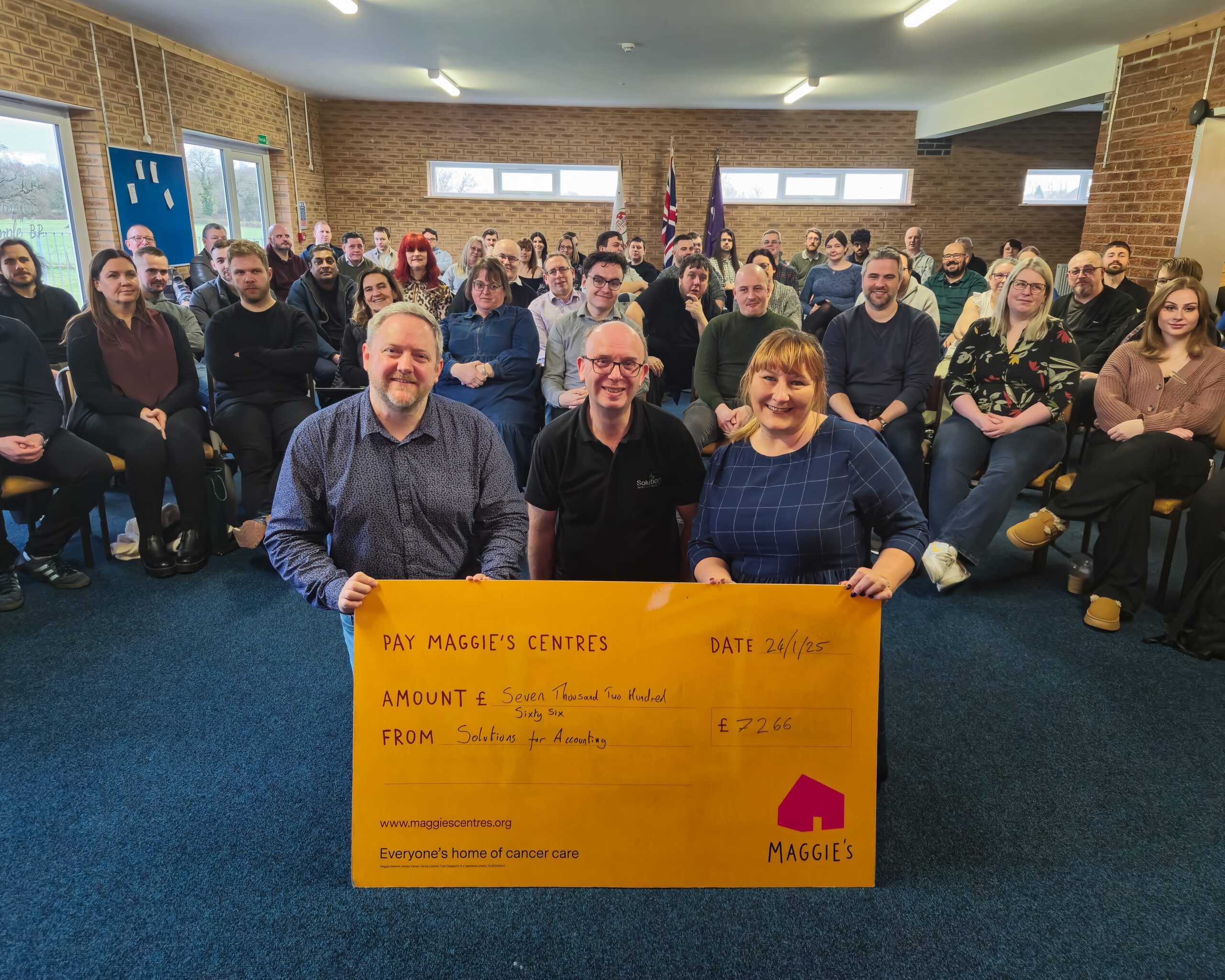 An image with a representative from Maggie's and two staff members holding a sign that shows how much Solutions raised for Maggie's last year