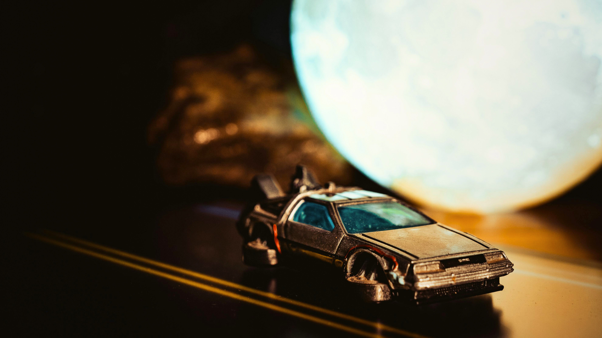 A toy DeLorean time machine is placed on a miniature road with a moon-shaped light in the background.
