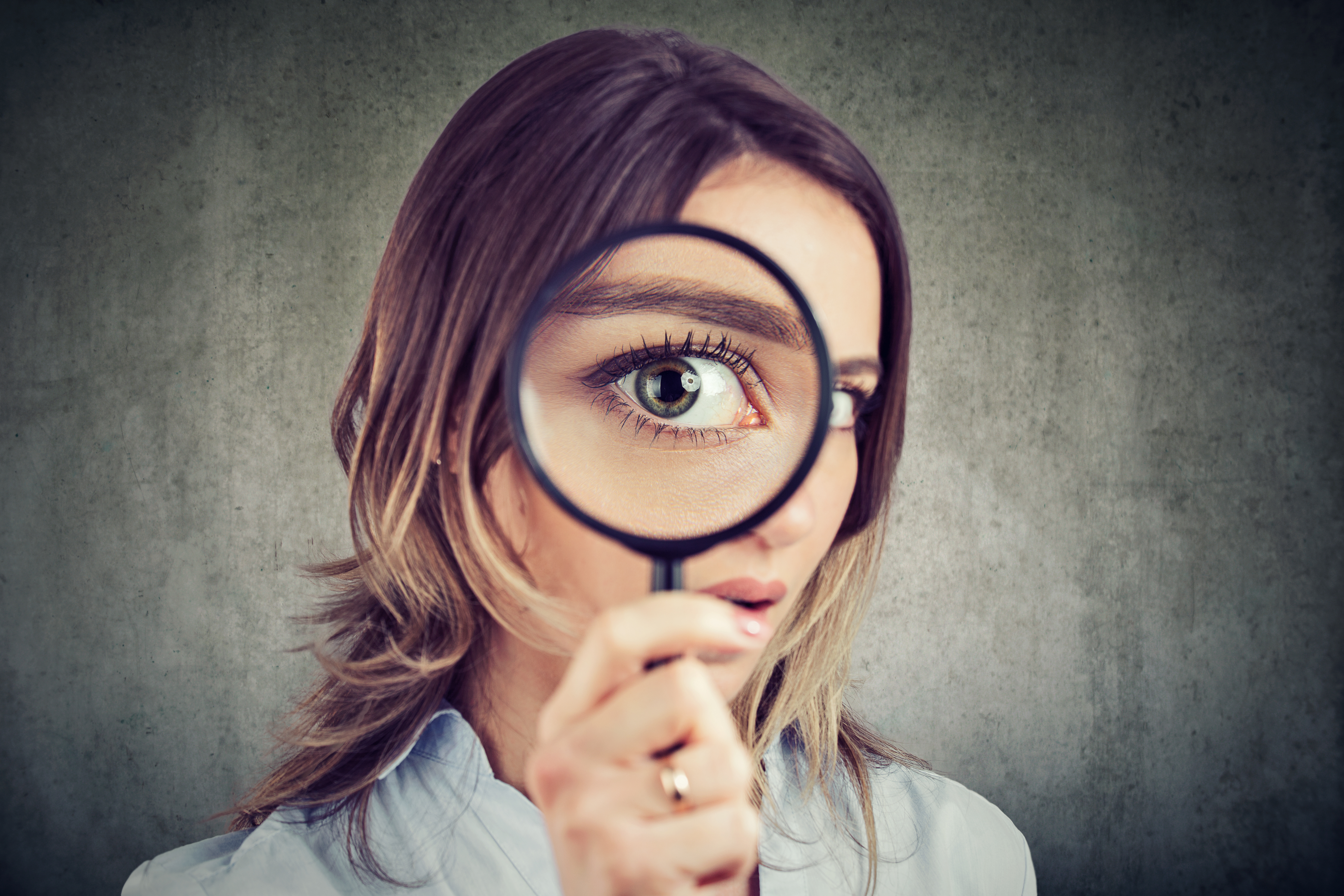 A young woman stares through a magnifying glass.