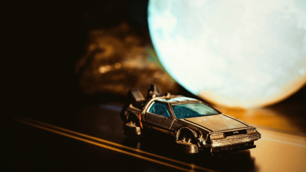 A toy DeLorean time machine is placed on a miniature road with a moon-shaped light in the background.