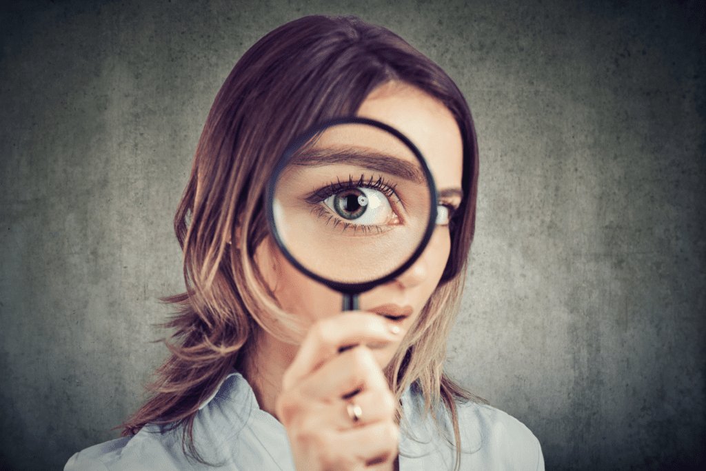 A young woman stares through a magnifying glass.