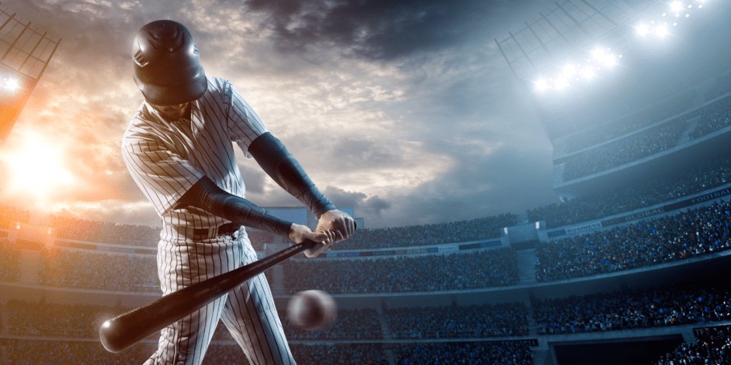 A baseball player swings his bat at a baseball in a busy stadium at sunset.