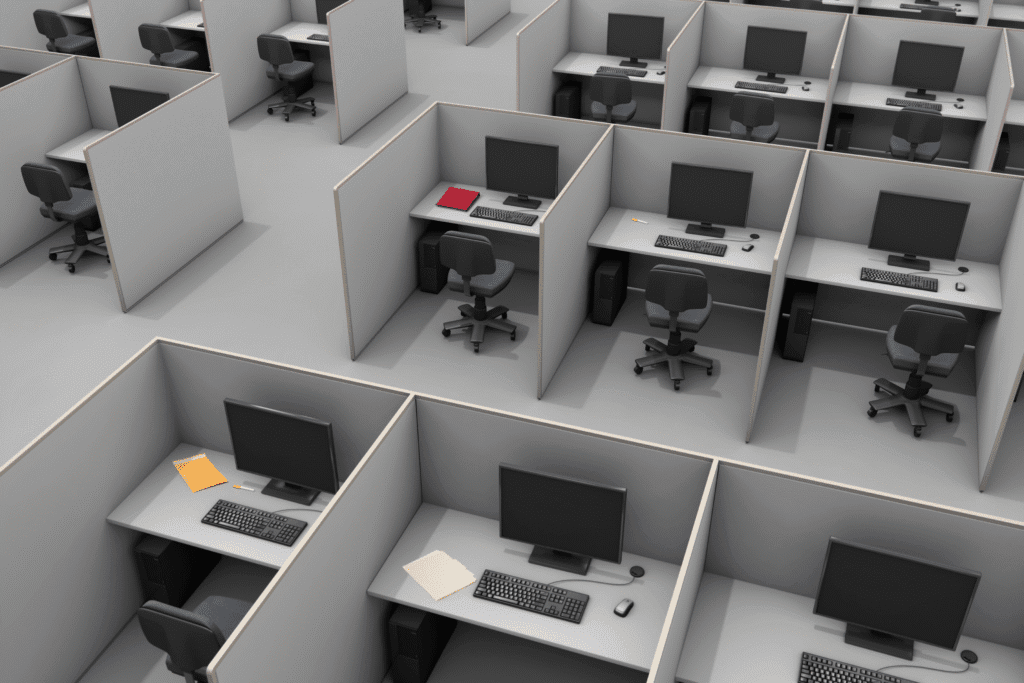 An elevated view of a bleak office space filled with tightly packed cubicles. Each cubicle is very narrow and contains a simple desk, computer, and desk chair.