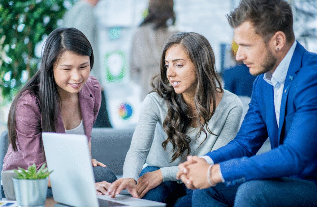 Three young office workers, two female and one male, sat down on a sofa looking at a laptop screen.