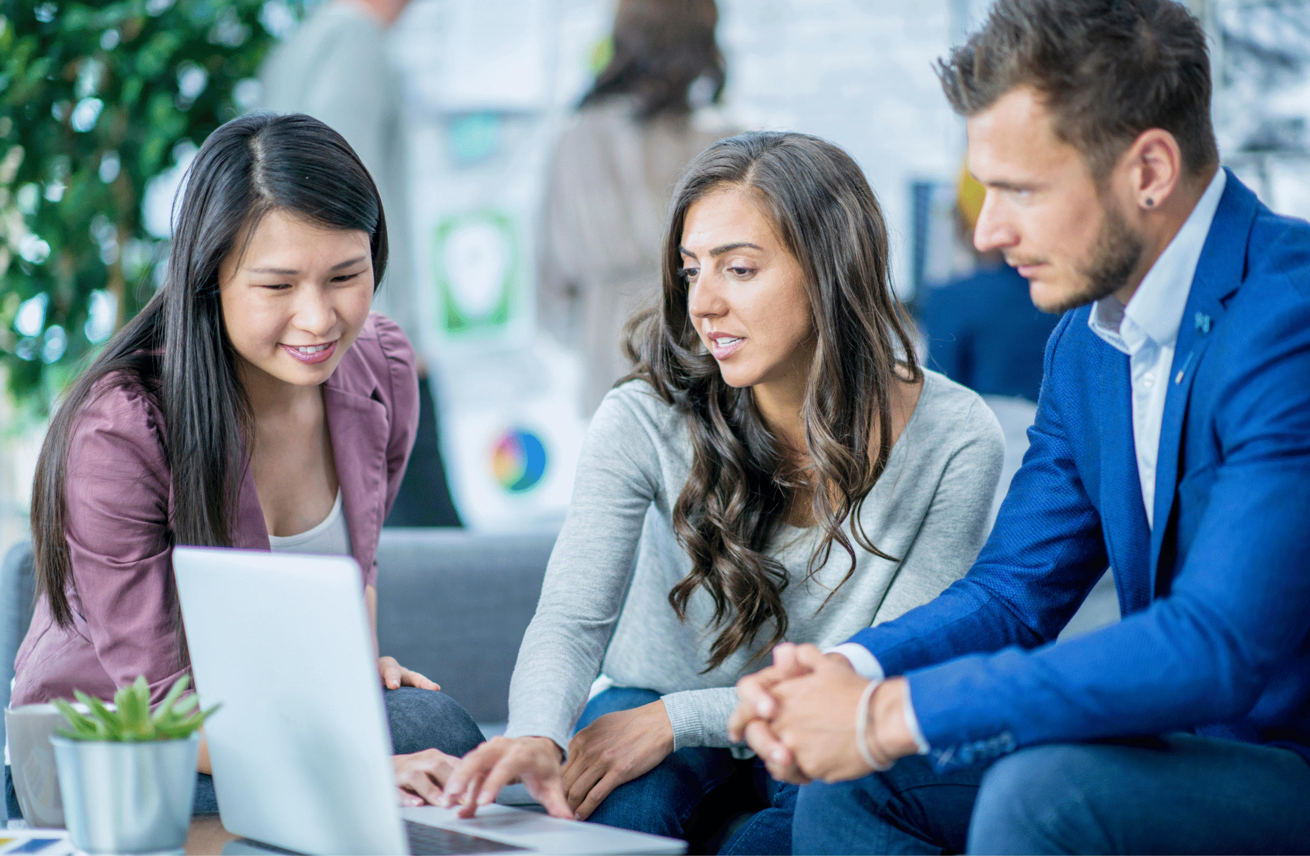 Three young office workers, two female and one male, sat down on a sofa looking at a laptop screen.
