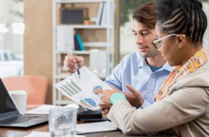 An image of two coworkers sat at a desk, reviewing the business' financial records. 