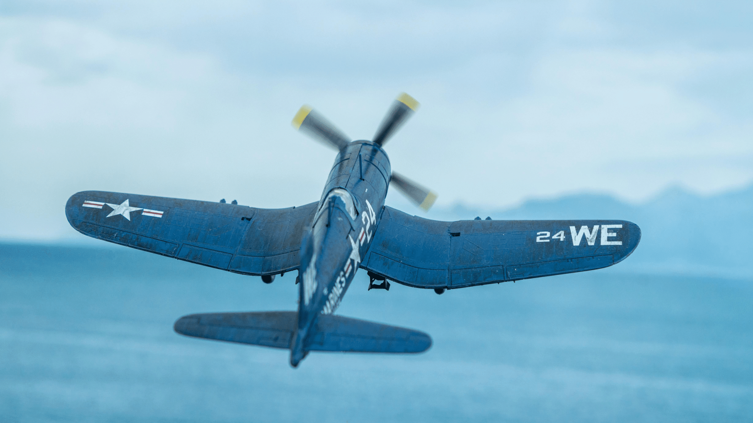 A World War Two fighter plane flies against a backdrop of the sea below and the blue sky above.