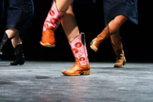 A close-up of people's legs on stage as they line dance with cowboy boots on.