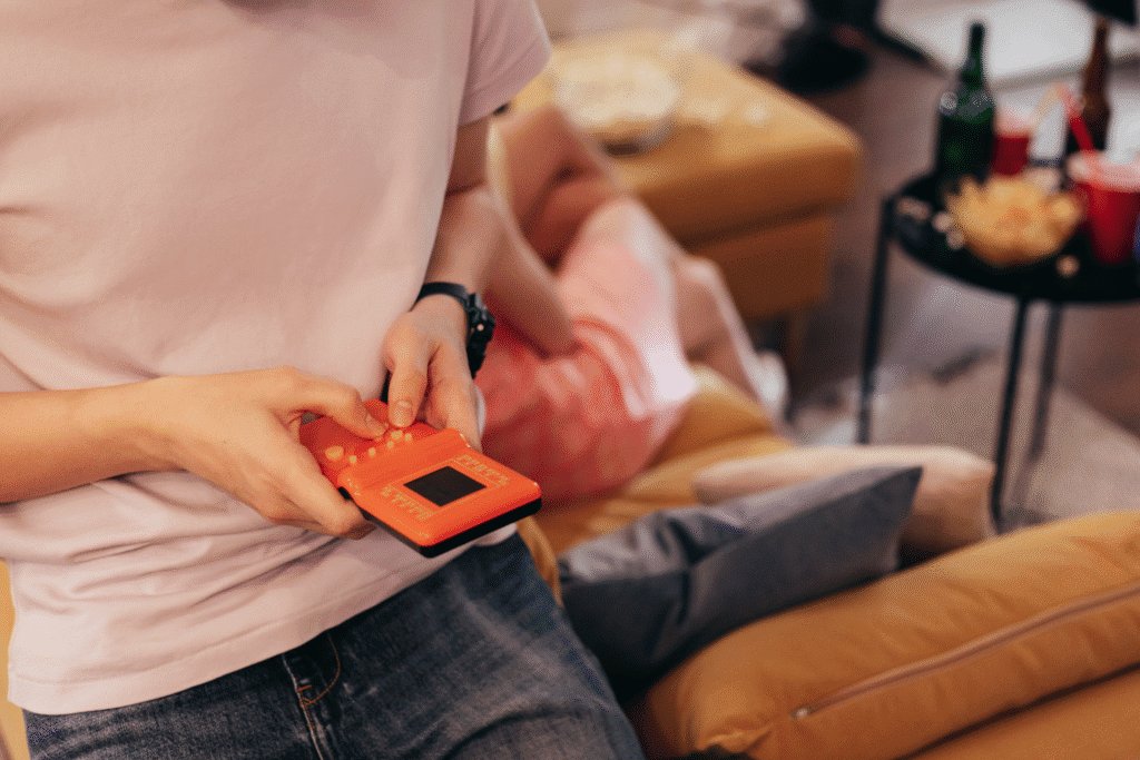 A medium shot of a person playing on a handheld video game console in a warm lounge room
