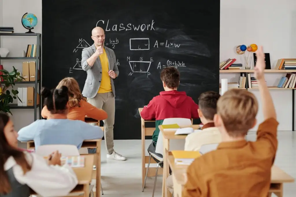 School classroom with a blackboard in the background and a child holding their hand up