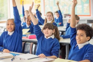School children sat in a classroom, raising their hands to answer a question.