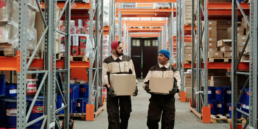 Two men carrying boxes through a warehouse