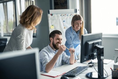 Three office workers stood around a desk working on a project.